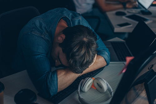 young exhausted programmer sleeping on keyboard at night in office