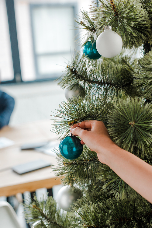 cropped view of woman touching christmas ball on christmas tree in office
