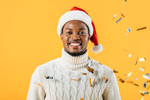 African American man in Santa hat smiling and  on yellow background with confetti