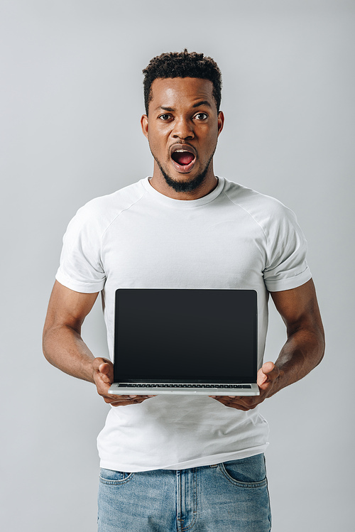 shocked African American man showing laptop with blank screen and  isolated on grey