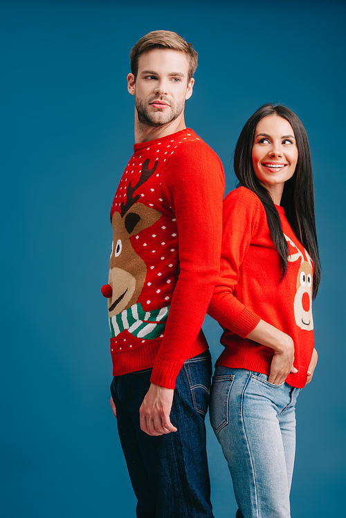 happy couple in christmas sweaters standing back to back isolated on blue