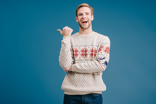 laughing man in winter sweater pointing at something isolated on blue
