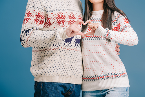 cropped view of couple in winter sweaters showing heart sign isolated on blue