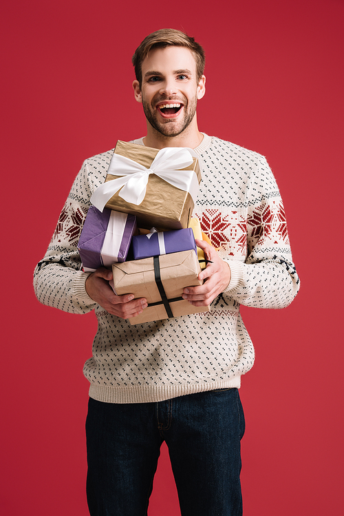 happy handsome man holding christmas gifts isolated on red