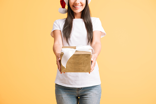 cropped view of smiling woman in santa hat holding christmas gift box isolated on yellow