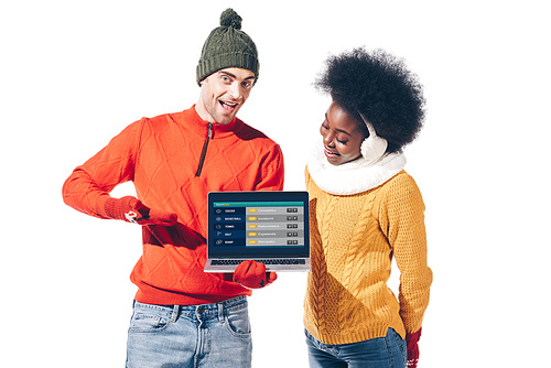 multicultural couple in winter sweaters, gloves and hat holding laptop with weather website, isolated on white