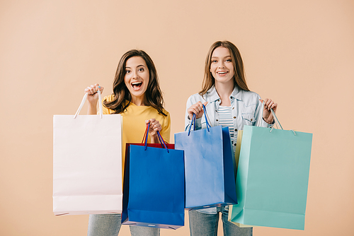 attractive and smiling friends holding shopping bags isolated on beige