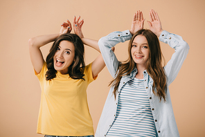 attractive and smiling friends showing bunny ears with hands isolated on beige