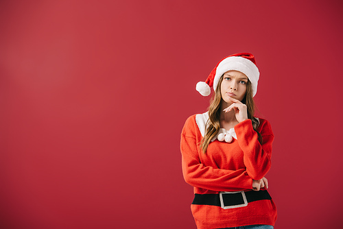 attractive and pensive woman in santa hat and sweater  isolated on red