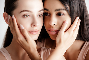 beautiful young multicultural girls in beige outfit tenderly touching each other faces isolated on white