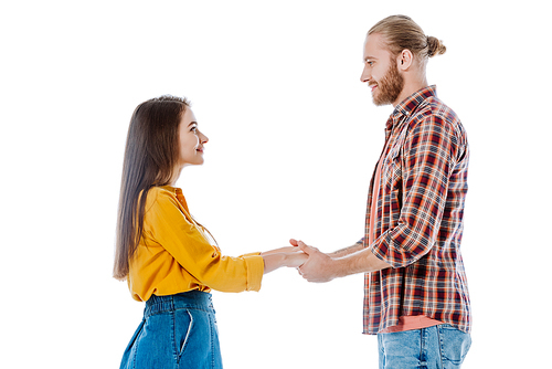 side view of young couple in casual outfit holding hands and looking at each other isolated on white