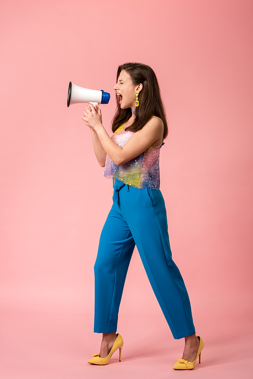 full length view of angry young stylish disco girl screaming in megaphone on pink