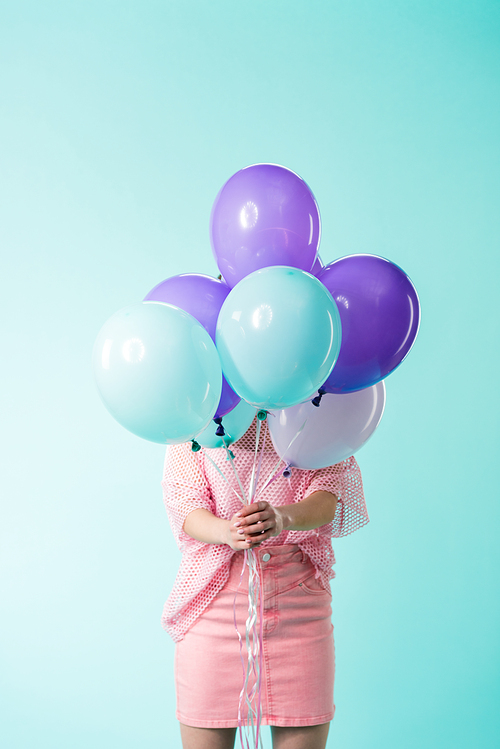 girl in pink outfit holding balloons in front of face isolated on turquoise