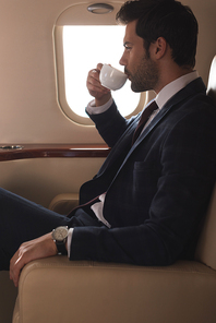 handsome businessman in suit drinking coffee in airplane during business trip