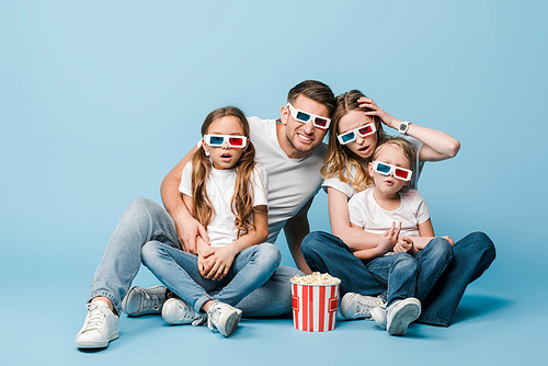 shocked family in 3d glasses watching movie and holding popcorn bucket on blue