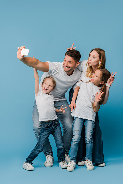 cheerful family showing victory signs while taking selfie on smartphone on blue