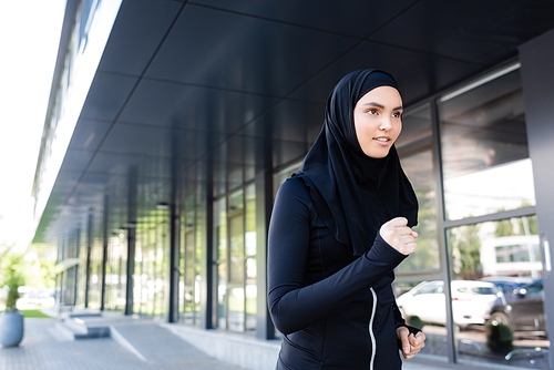 young muslim sportswoman in hijab running near building