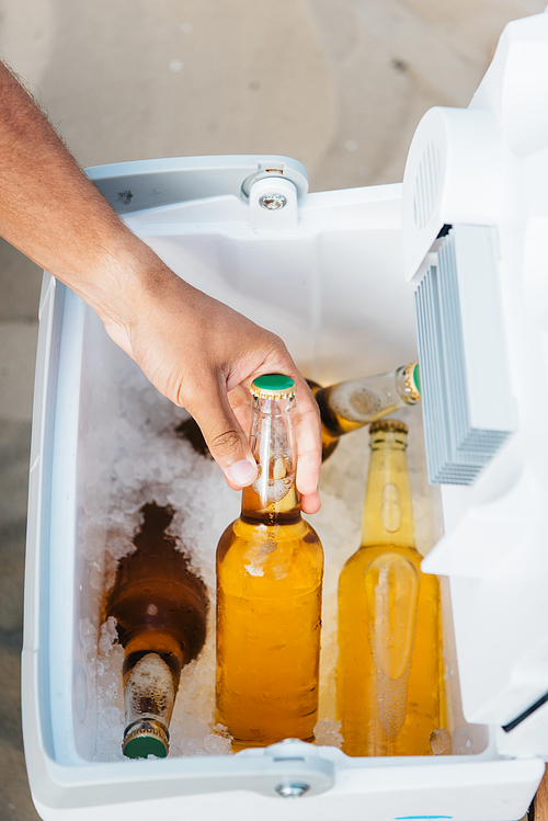 cropped view of young man taking bottle of beer from portable fridge