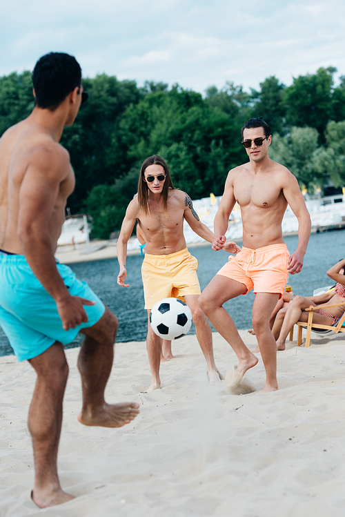 handsome, young multicultural men playing football on beach