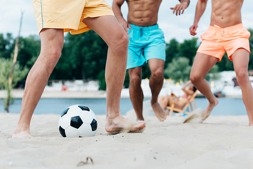 cropped view of young multicultural men playing football on beach