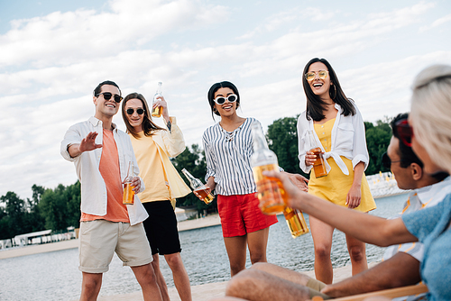 cheerful, young multicultural friends having fun and drinking beer on beach