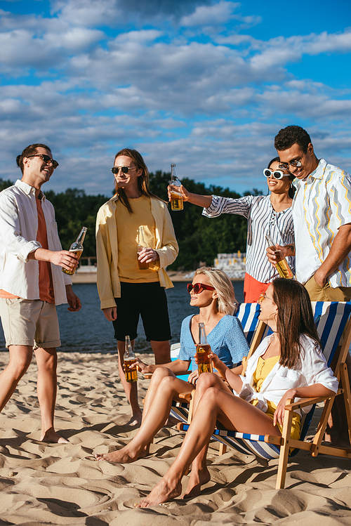 cheerful multicultural friends talking while drinking beer on beach