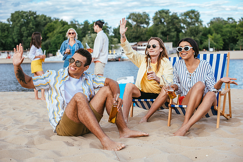 handsome multicultural men waving hands while having fun with friends on beach