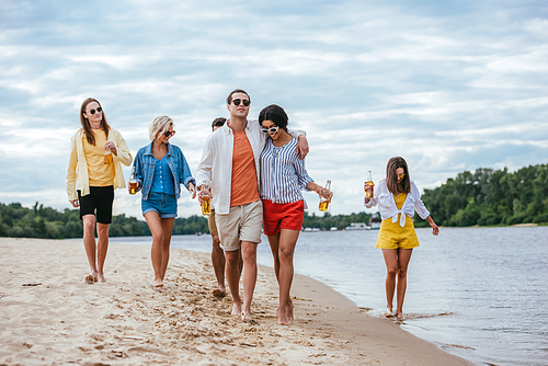 interracial couple hugging while walking on riverside together with multicultural friends