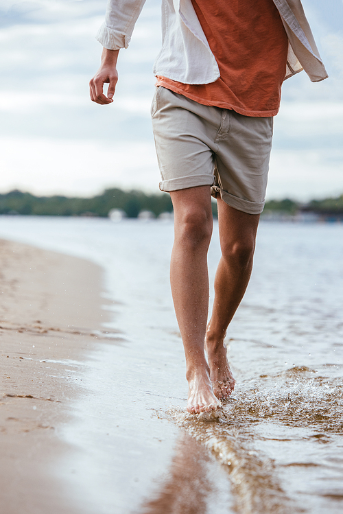 cropped view of young man in shorts running on riverside