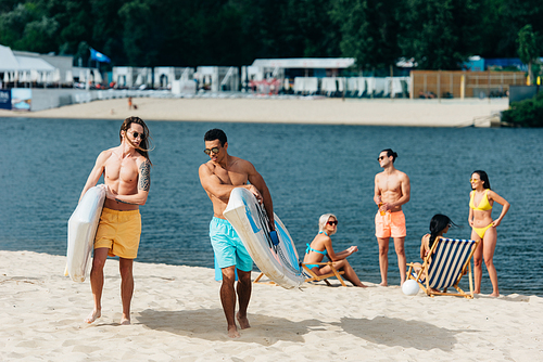 handsome multicultural men walking on beach and holding surfing boards