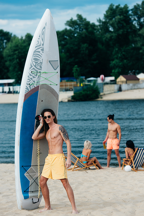 handsome young man looking standing near surfboard on beach and 