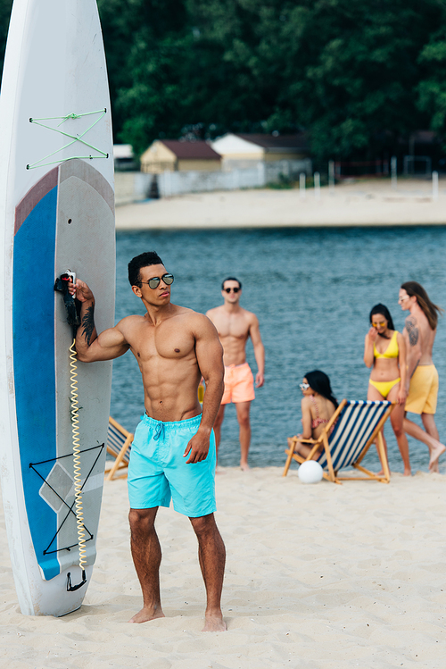 handsome mixed race man  while standing near surfboard on beach