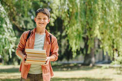 smiling schoolboy  while standing in park and holding books