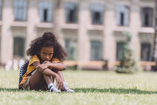 upset african american schoolgirl  while sitting on lawn