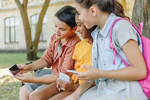 cute schoolboy showing smartphone with blank screen to multicultural schoolgirls