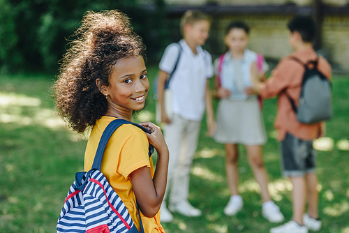 selective focus of adorable african american schoolgirl smiling at camera near multiethnic friends