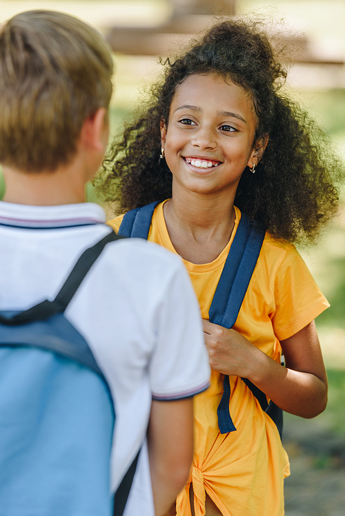 back view of schoolboy standing near smiling african american schoolgirl