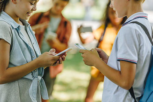 selective focus of schoolkids using smartphones while standing near multicultural friends