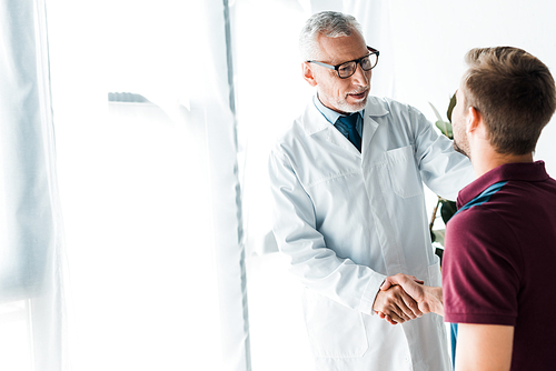 happy doctor in glasses shaking hands with man in clinic