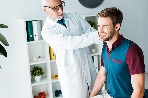 bearded chiropractor in white coat and glasses touching happy patient in clinic