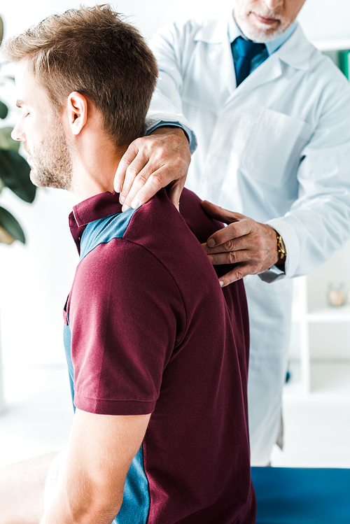 cropped view of chiropractor in white coat touching back of patient with closed eyes