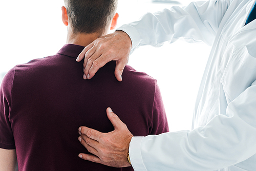 cropped view of chiropractor in white coat touching back of patient in clinic