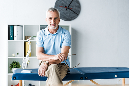 cheerful man sitting on massage table and holding glasses