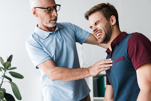 bearded man in glasses touching patient with pain in clinic