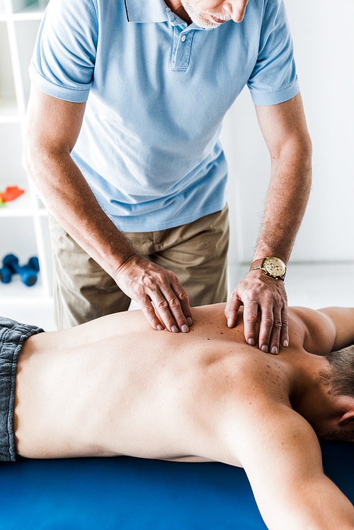 cropped view of bearded chiropractor doing massage to patient on massage table