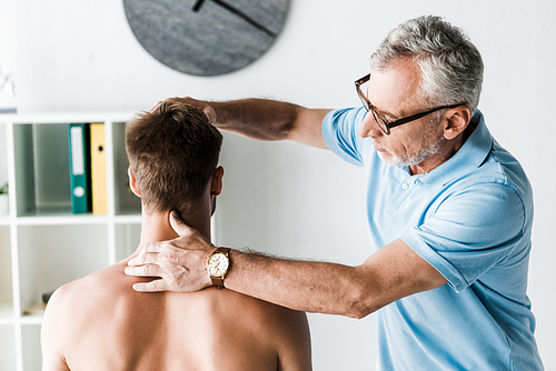 bearded doctor in glasses touching neck of shirtless patient sitting in clinic