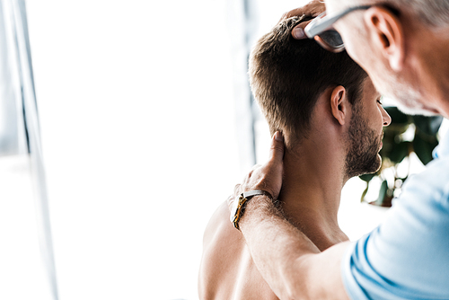 selective focus of doctor touching neck of shirtless man sitting in clinic