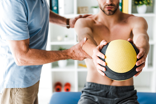 cropped view of doctor standing near patient working out with ball