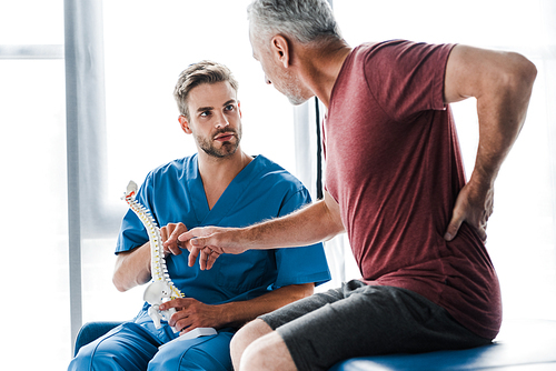 selective focus of doctor holding spine model and looking at patient gesturing while touching back