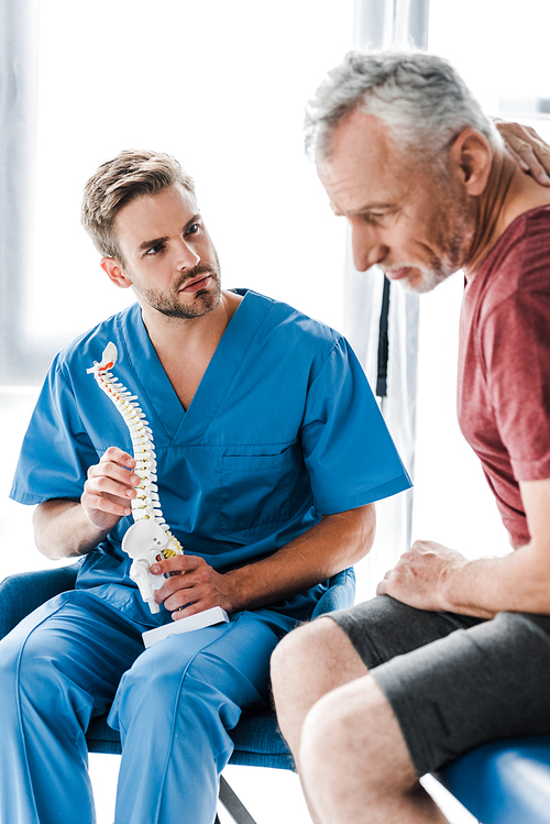 selective focus of doctor holding spine model and looking at patient